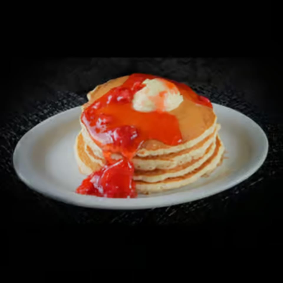 Stack of golden pancakes topped with strawberry syrup and a dollop of butter on a white plate.