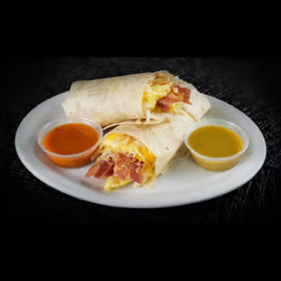 Two breakfast burritos filled with scrambled eggs and bacon, served with two dipping sauces.