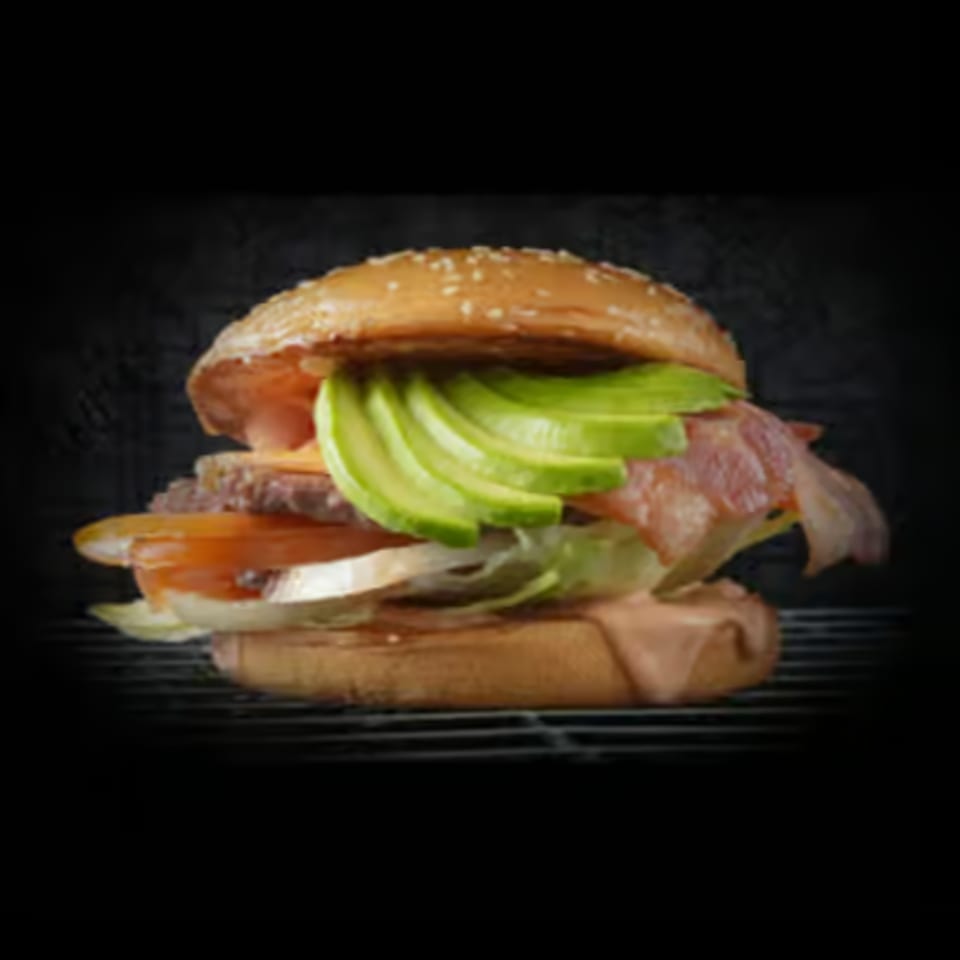A gourmet burger with avocado, bacon, cheese, tomato, onion, and lettuce on a sesame bun.
