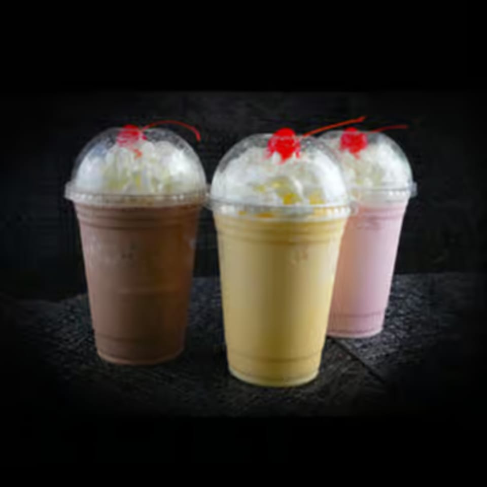 Three milkshakes in clear cups: chocolate, vanilla, and strawberry, topped with whipped cream and cherries.